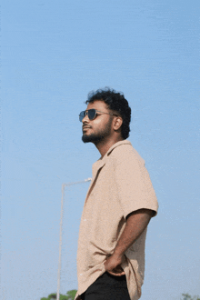 a man wearing sunglasses and a tan shirt is standing in front of a blue sky