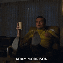 a man is sitting in a chair and pointing with the name adam morrison below him