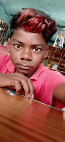 a young boy with red hair is sitting at a table with his hand on his chin .