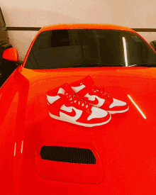 a pair of red and white nike shoes sitting on the hood of a red car