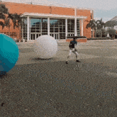 a man in a baseball uniform stands in front of a large building with a large white ball in the middle of it