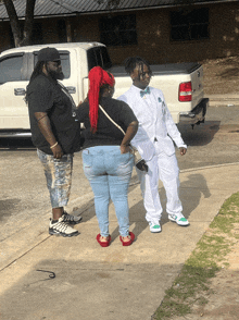 a man in a white suit stands next to a woman and a man with dreadlocks