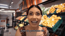 a woman in a grocery store says ajde da probamo 89 in front of a display of fruits and vegetables