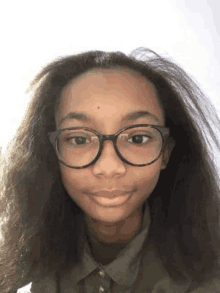 a young girl wearing glasses and a green shirt is looking at the camera .