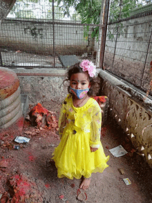 a little girl wearing a yellow dress and a mask