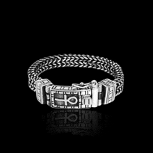 a silver bracelet with a cross on it is on a black surface .