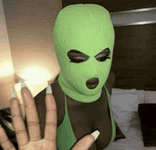 a woman wearing a green ski mask and a green tank top is standing on a bed .