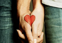 a man and a woman hold hands with a red heart painted on their wrists