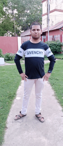 a man wearing a givenchy shirt stands with his hands in his pockets