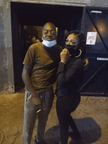 a man wearing a mask stands next to a woman wearing a mask in front of a sign that says no smoking