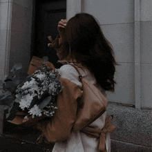 a woman in a trench coat is holding a bouquet of flowers in her hand .