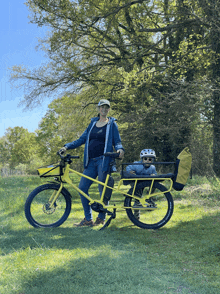 a woman is standing next to a yellow bike with a child in the back seat