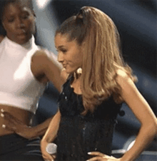 a woman in a black dress is standing next to another woman in a white crop top