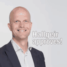 a bald man in a suit is smiling with the words halligeir approves behind him