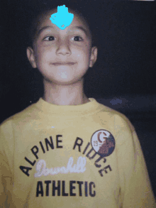 a young boy is wearing a yellow alpine ridge downhill athletic shirt