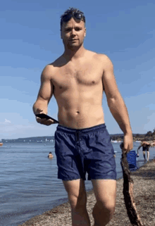 a shirtless man in blue shorts is walking on the beach holding a stick