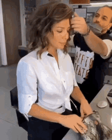 a woman in a white shirt is getting her hair done by a man wearing a black shirt that says " tutto teatro "