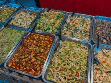 a variety of food in trays with spoons on a table .