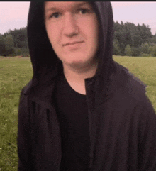 a man wearing a hooded jacket and a black shirt is standing in a field .