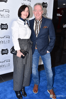 a man and a woman are standing on a blue carpet in front of a sign that says " super ecran "