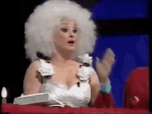 a woman wearing a white wig and a white dress is clapping .