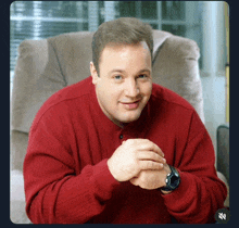 a man wearing a red sweater and a watch sits in a chair