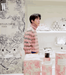 a man in a pink sweater is standing in front of a wall that says christian dior