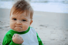 a baby in a green and white shirt holds his fist up