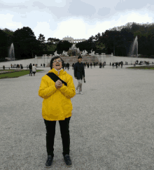 a woman in a yellow jacket stands in front of a large fountain