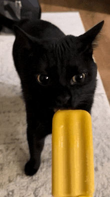 a black cat is eating a yellow popsicle on a rug