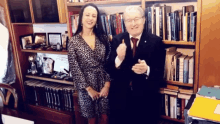 a man and a woman are posing for a picture in front of a bookshelf with a book titled steve jobs