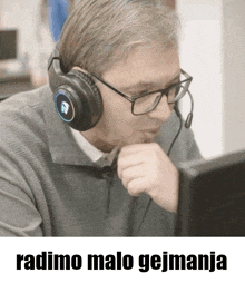 a man wearing headphones and glasses is looking at a computer screen with the caption radimo malo gejmanja