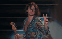 a man wearing a colorful shirt is holding a guitar and giving a peace sign