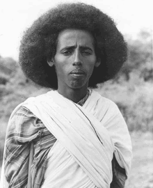 a black and white photo of a man with an afro and a white cloth around his neck .