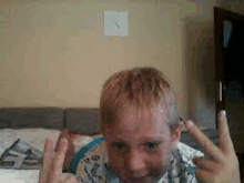 a young boy is sitting on a bed making a funny face and giving the middle finger .