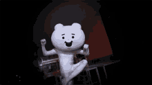 a white teddy bear mascot is standing on one leg in a dark room