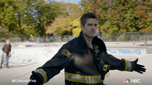 a man in a fireman 's uniform is standing with his arms outstretched in front of a skate park with graffiti on it