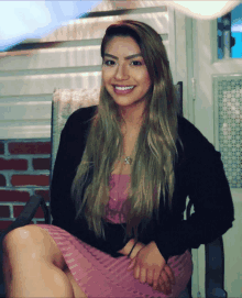 a woman in a pink dress sits in a chair smiling