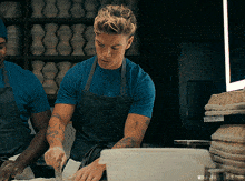 a man in a blue shirt is preparing food in front of a sign that says ' bread ' on it