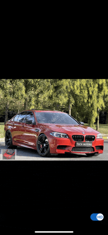 a red bmw is parked in front of a park