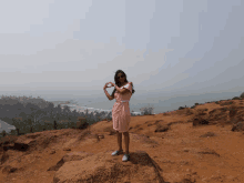 a woman in a pink dress stands on a rock making a heart shape