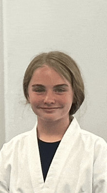 a young girl wearing a white karate uniform is smiling for the camera