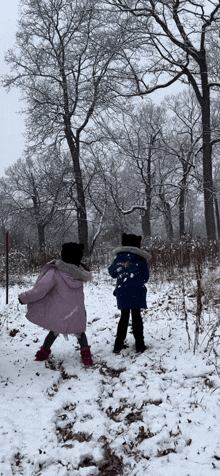 two girls are walking through the snow looking at trees