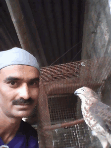 a man standing next to a bird in a cage and wearing a hat