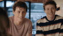 two young men with curly hair are smiling and wearing striped sweaters