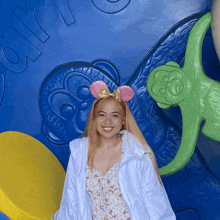 a woman wearing a white jacket and pink mouse ears stands in front of a blue wall with the word air on it