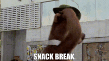 a man wearing a hat and sunglasses is standing in front of a building with the words `` snack break '' written on it .