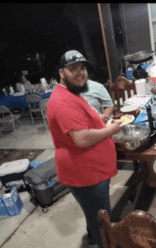 a man in a red shirt is holding a plate of food in front of a table