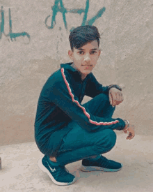 a young man is squatting down in front of a wall with graffiti .