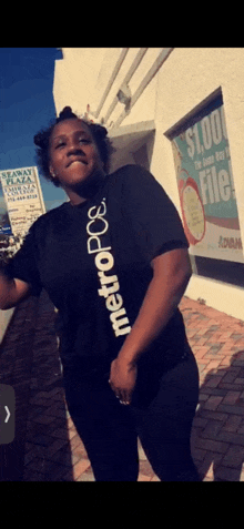 a woman wearing a black metropcs t-shirt is standing in front of a building